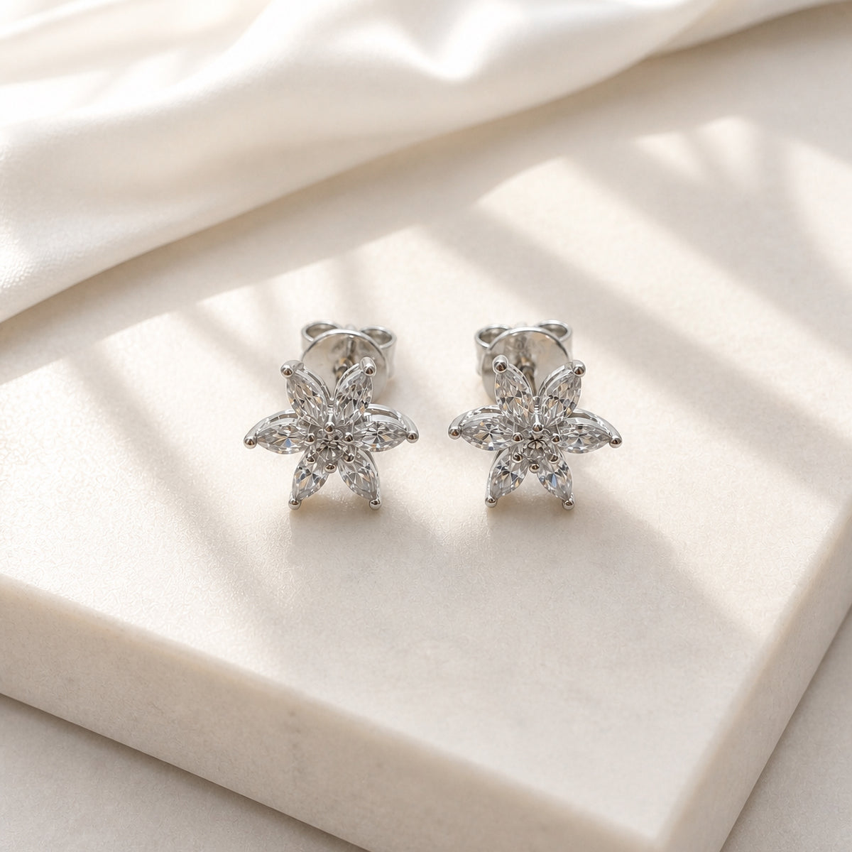 Pair of silver star-shaped earrings on a light beige fabric background
